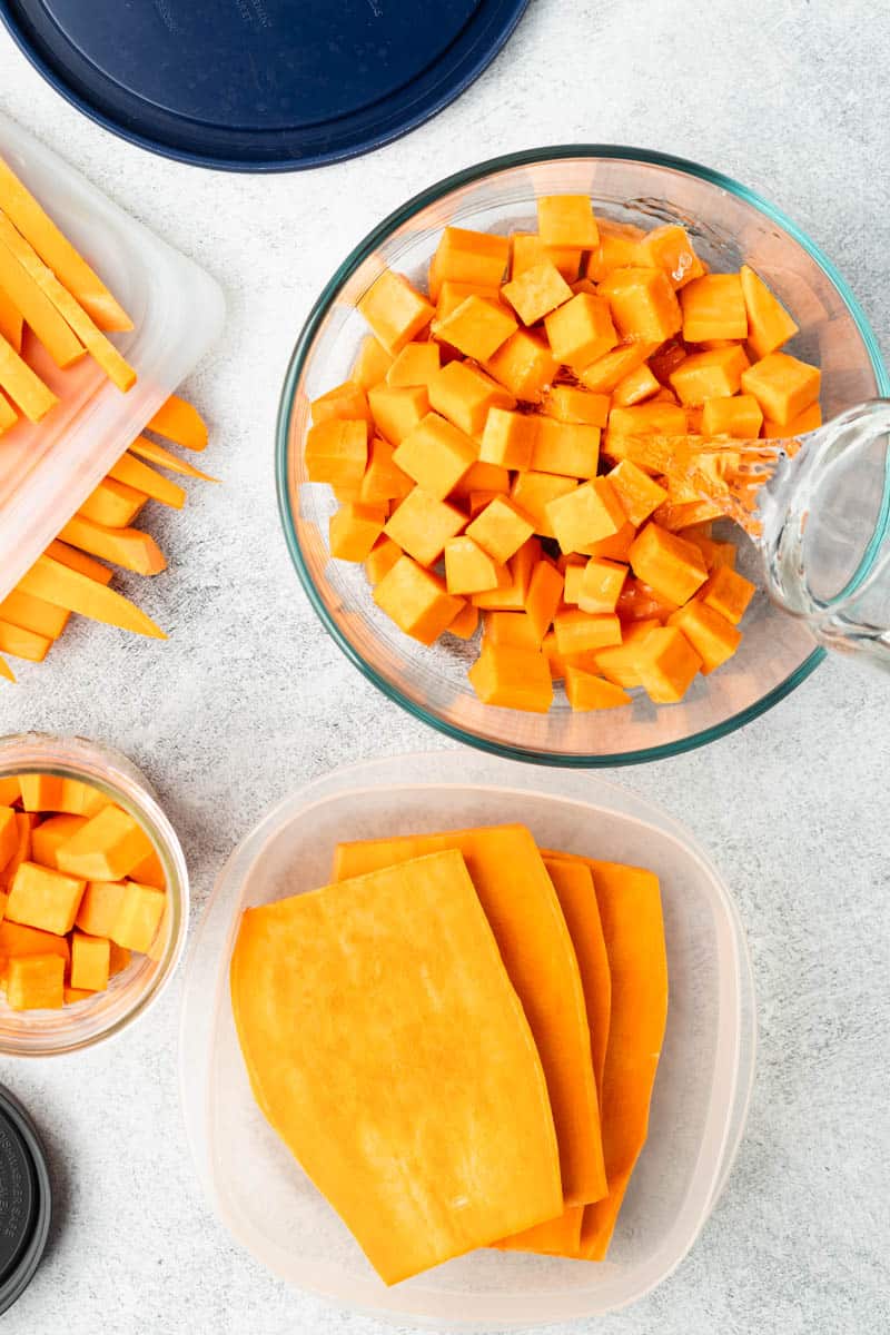 Sliced, cubed, and cut sweet potatoes are in separate storage containers on a textured grey counter.