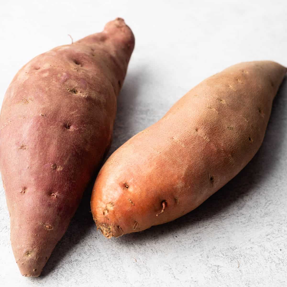 Two whole sweet potatoes are on a grey textured countertop.