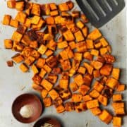 Crispy oven-roasted sweet potatoes are on a baking sheet next to a metal spatula.