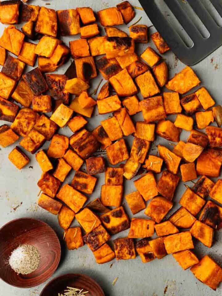 Crispy oven-roasted sweet potatoes are on a baking sheet next to a metal spatula.