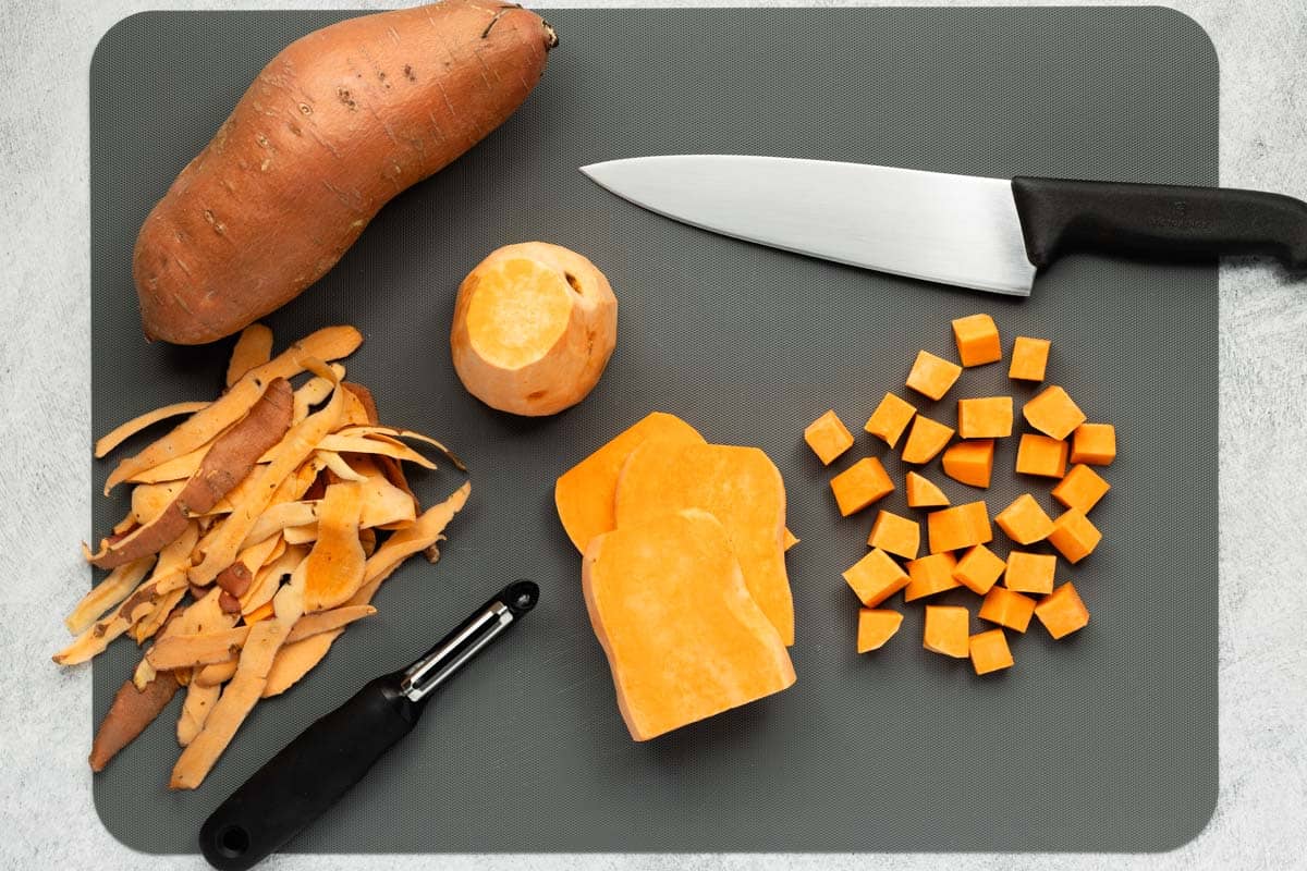 Preparing the sweet potatoes on a cutting board with potato peeler and chef's knife.