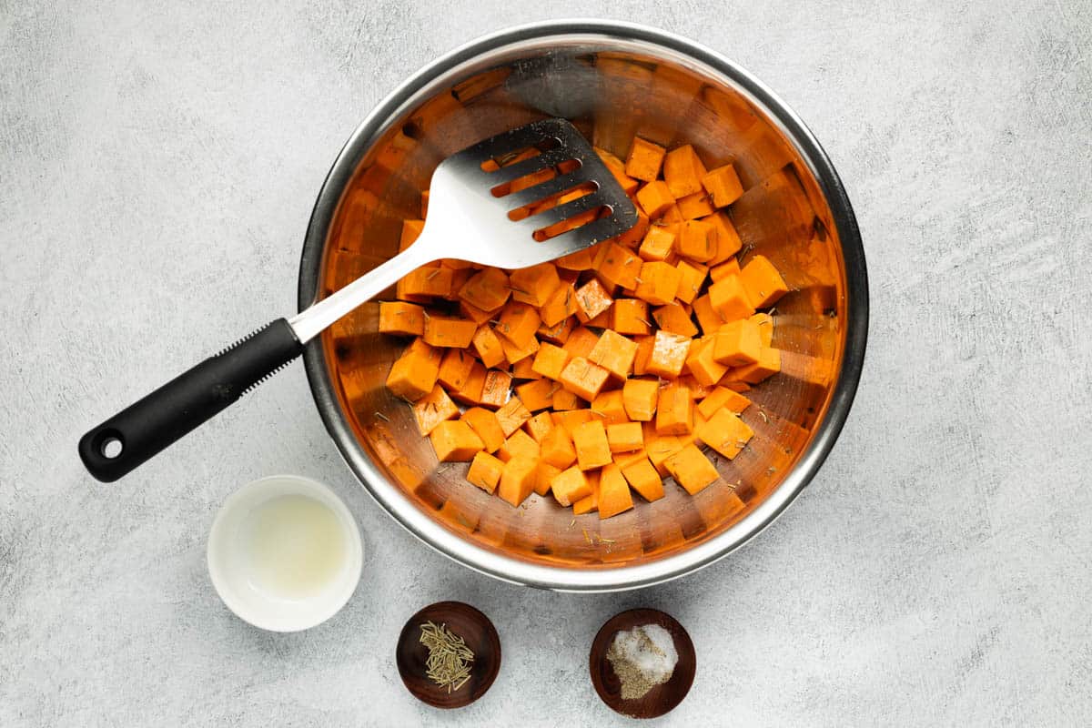 Cubed sweet potatoes in a mixing bowl are combined with the rest of the recipe ingredients.