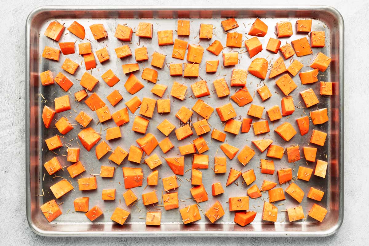 Seasoned sweet potato cubes are spread out on a baking sheet.