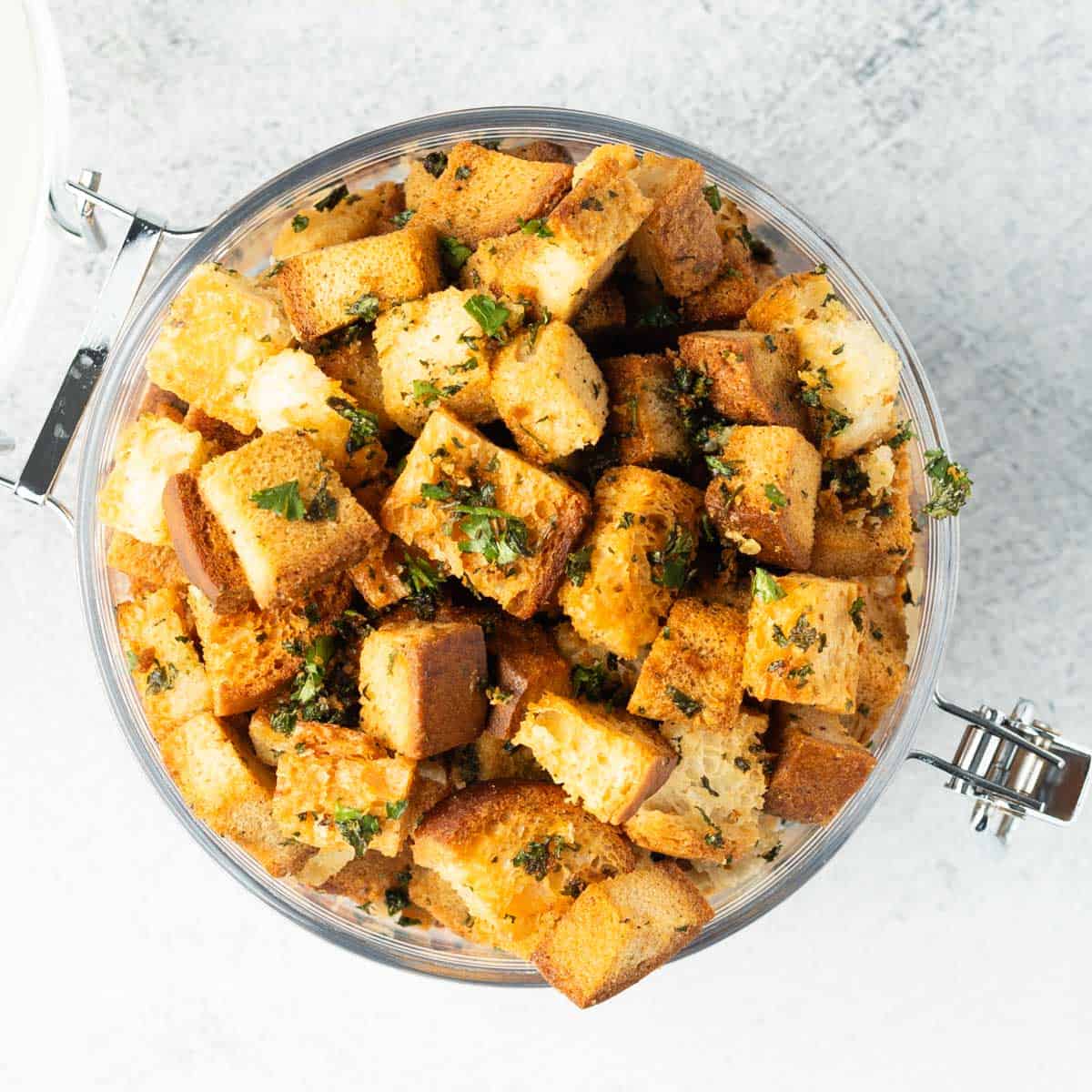 Top-down view of croutons in a clear plastic jar with lid.