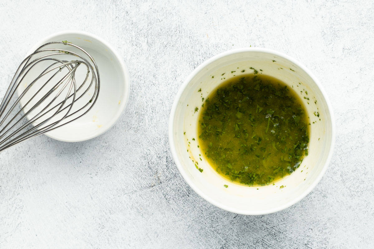 Butter and seasonings combined in a white mixing bowl using a whisk.