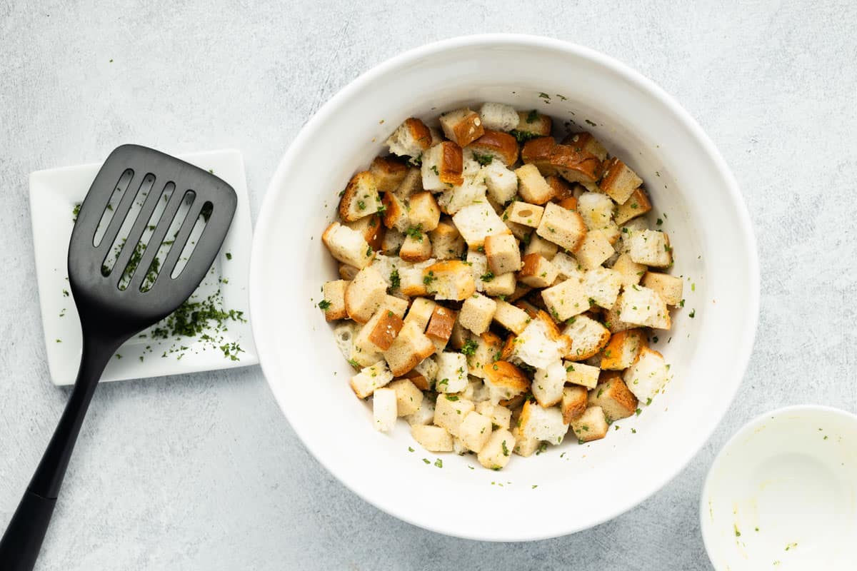 Cubed bread combined with butter and seasonings in a white mixing bowl.