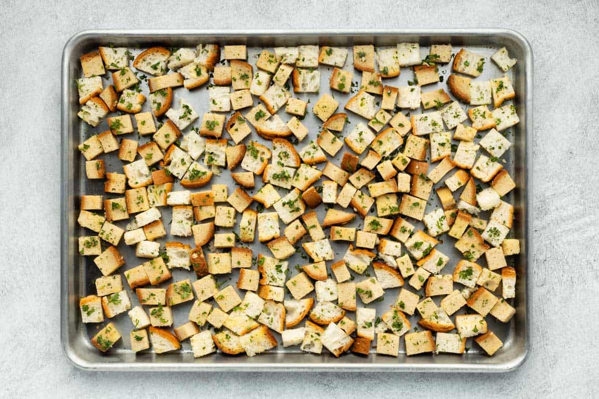 Seasoned bread cubes spread on a baking sheet.