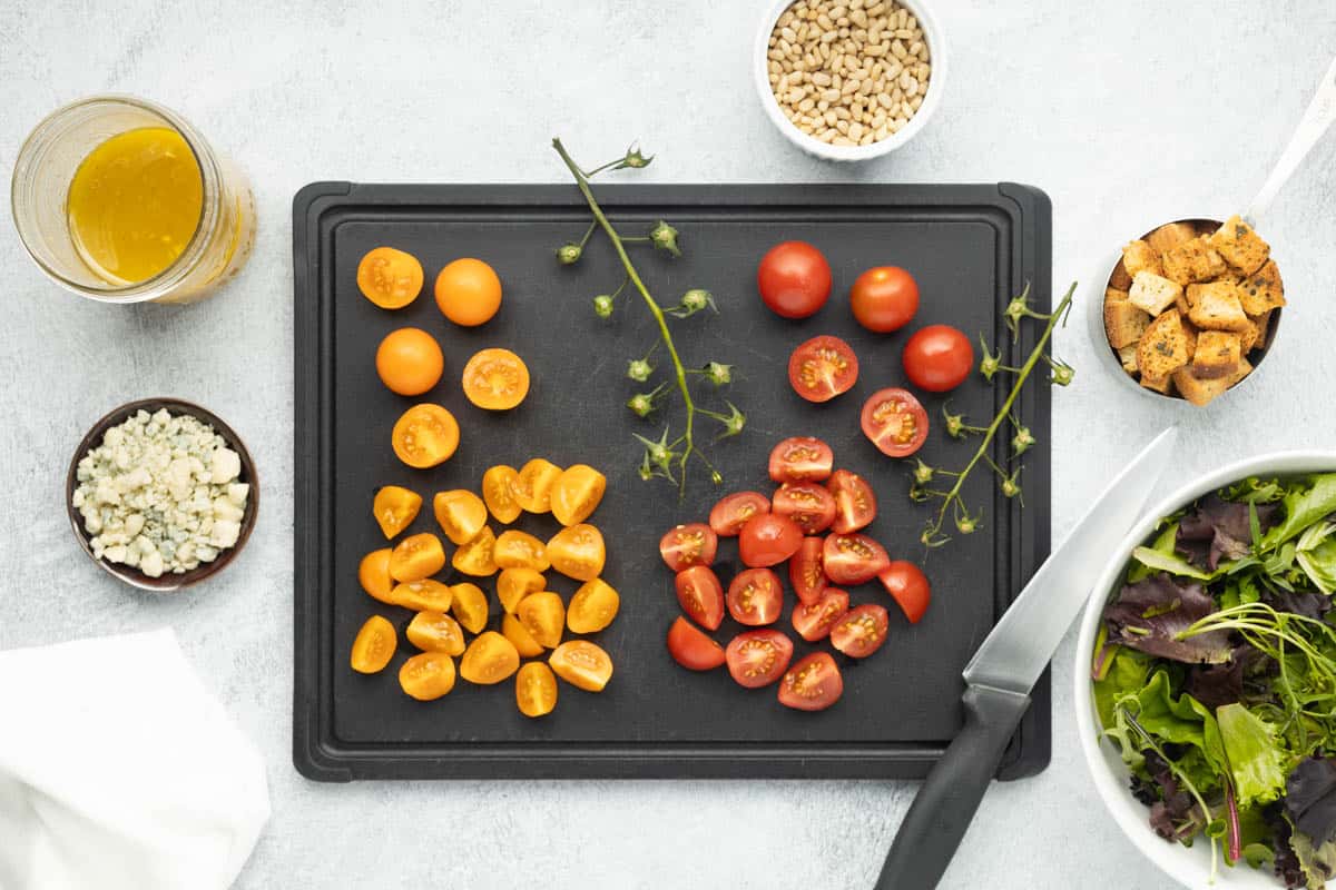 Chopped cherry tomatoes on a black cutting board.