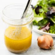 White wine vinaigrette in a mason jar next to a plate of mixed green salad.