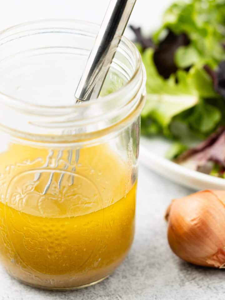 White wine vinaigrette in a mason jar next to a plate of mixed green salad.