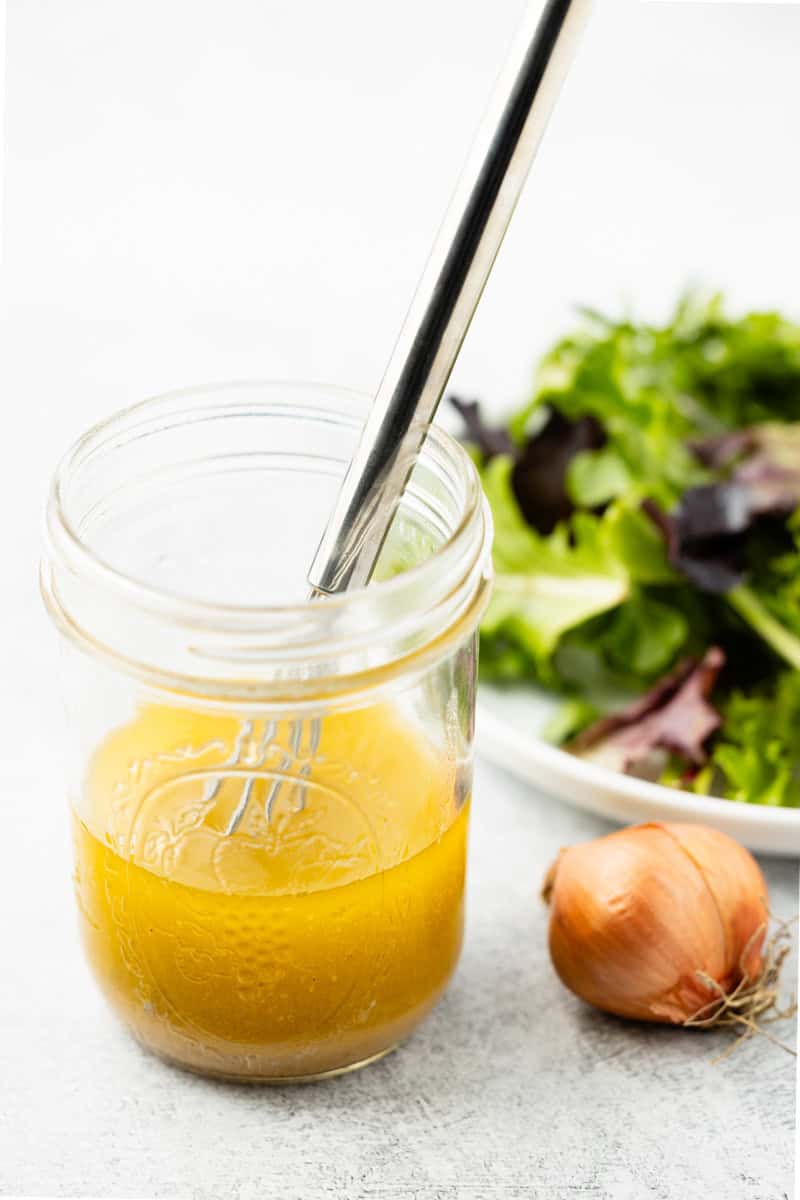 White wine vinaigrette in a mason jar next to a plate of mixed green salad.