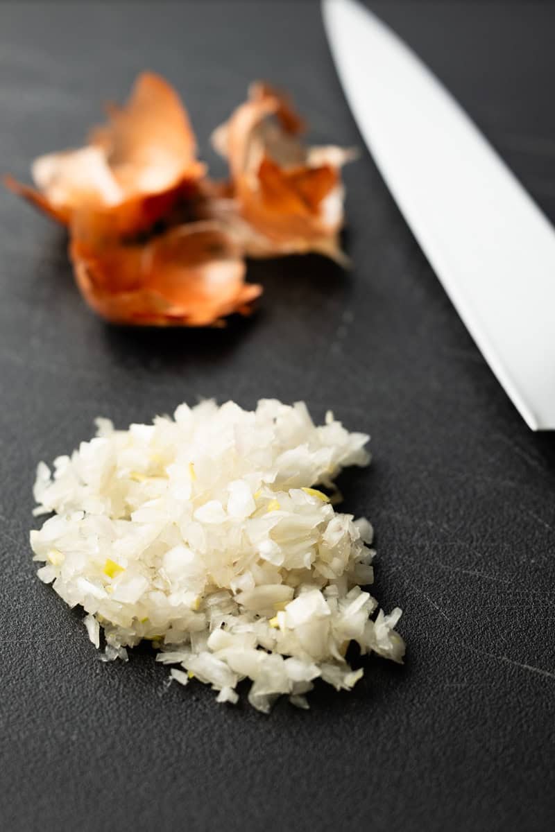 Chopped shallot on a black cutting board next to a chef's knife.