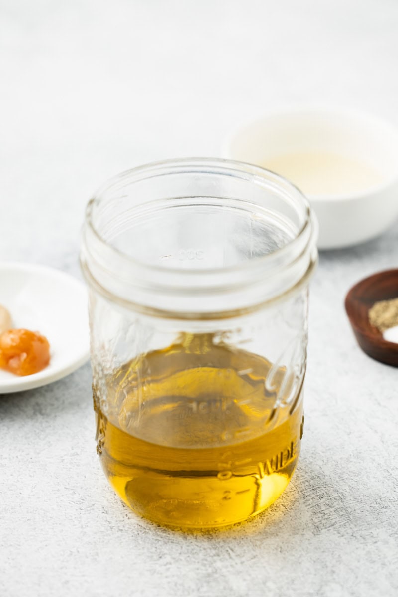 Mason jar filled with olive oil with other ingredients in the background.