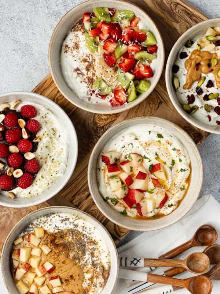 Five bowls of Greek yogurt with different toppings.