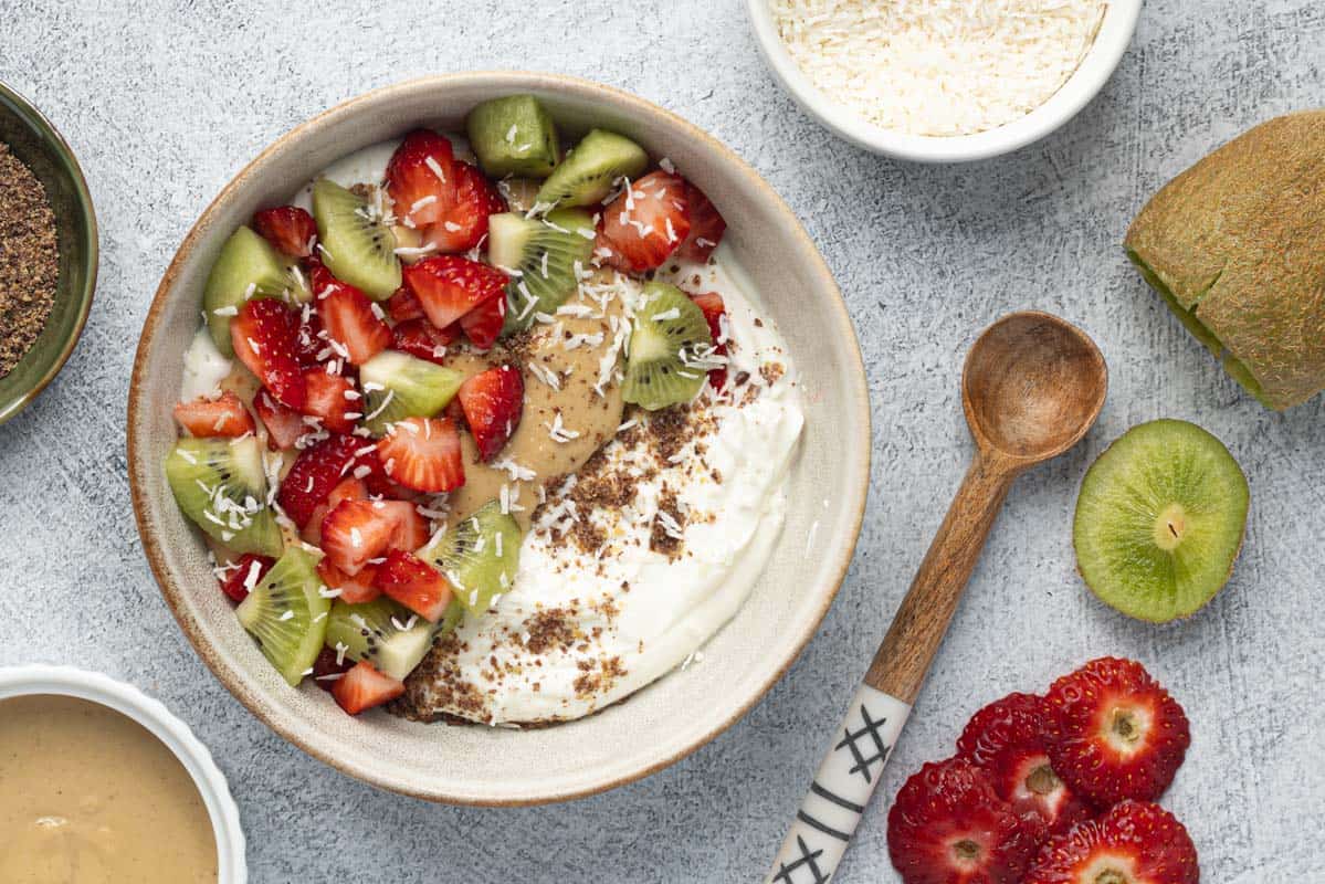 Greek yogurt bowl topped with kiwi, strawberries, cashew butter, and shredded coconut.