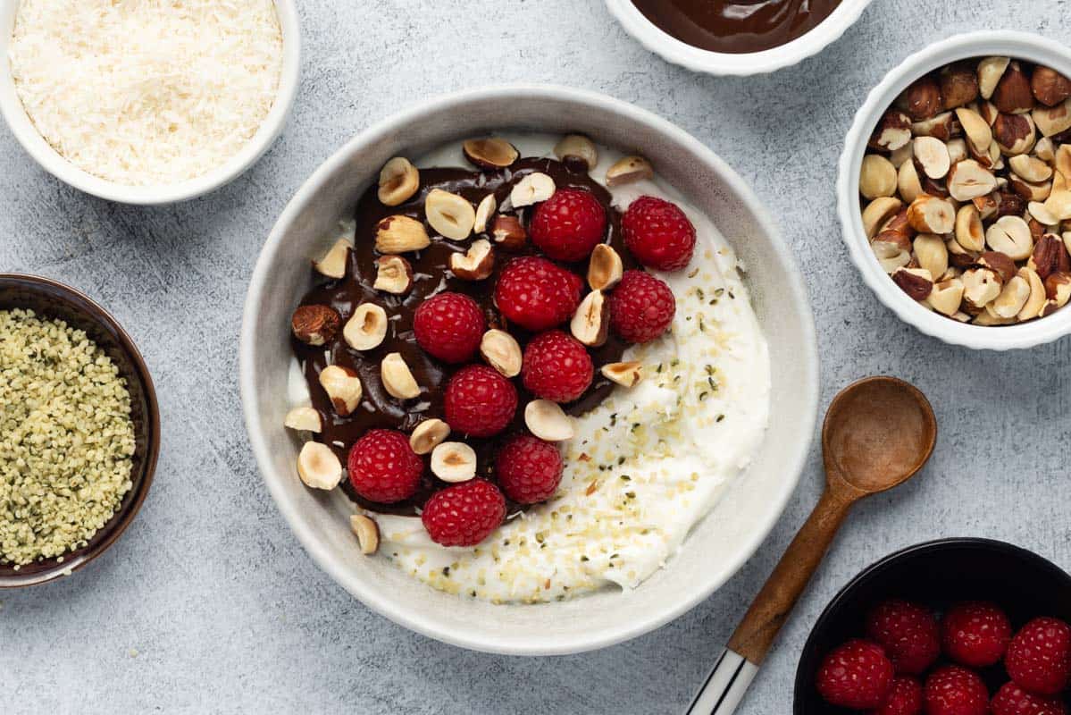 Greek yogurt bowl topped with chocolate sauce, raspberries, and hazelnuts.