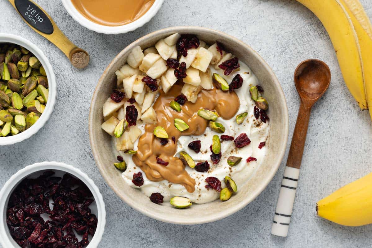 Greek yogurt bowl topped with almond butter, chopped banana, dried cranberries, and pistachios.