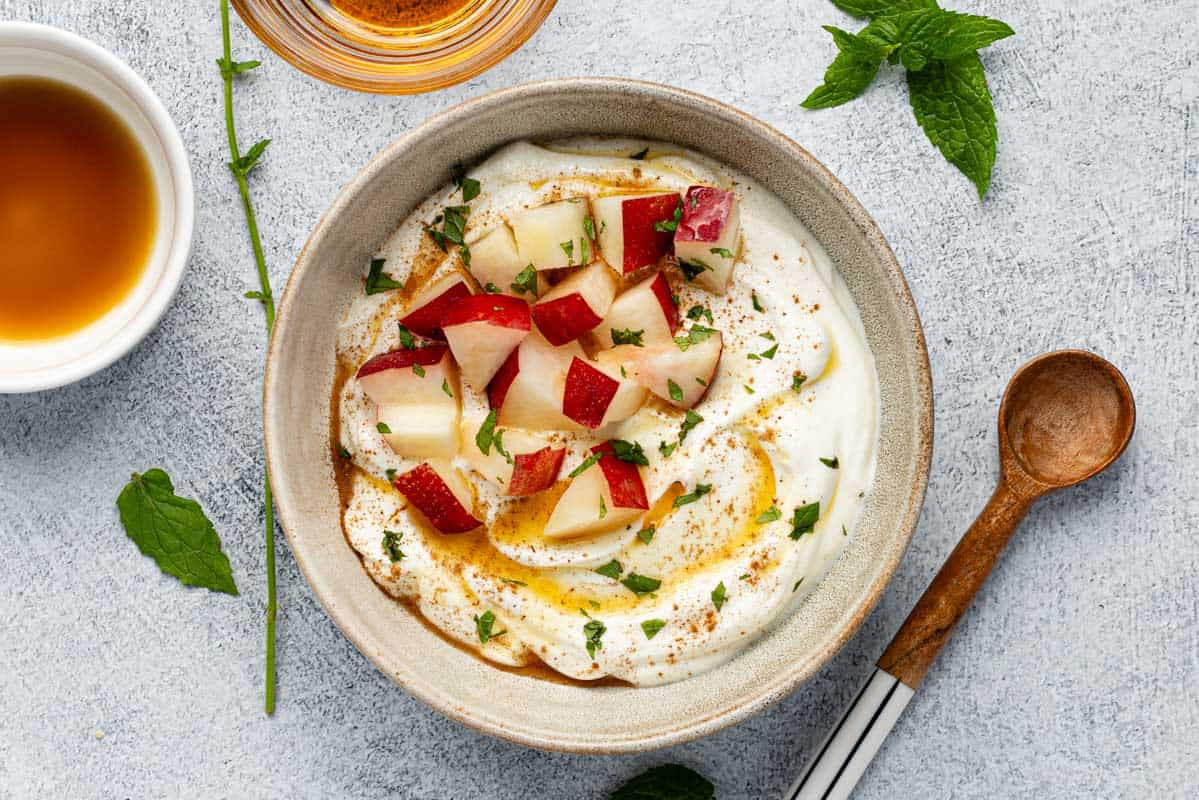 Greek yogurt bowl topped with chopped nectarine, maple syrup, and chopped mint.