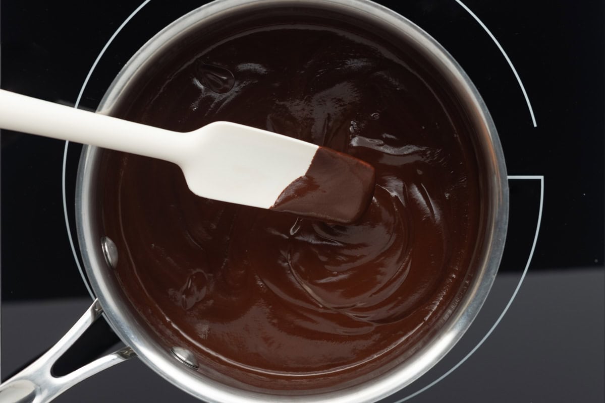 Almond milk and chocolate chips in a small saucepan fully melted into a shiny dark chocolate sauce.