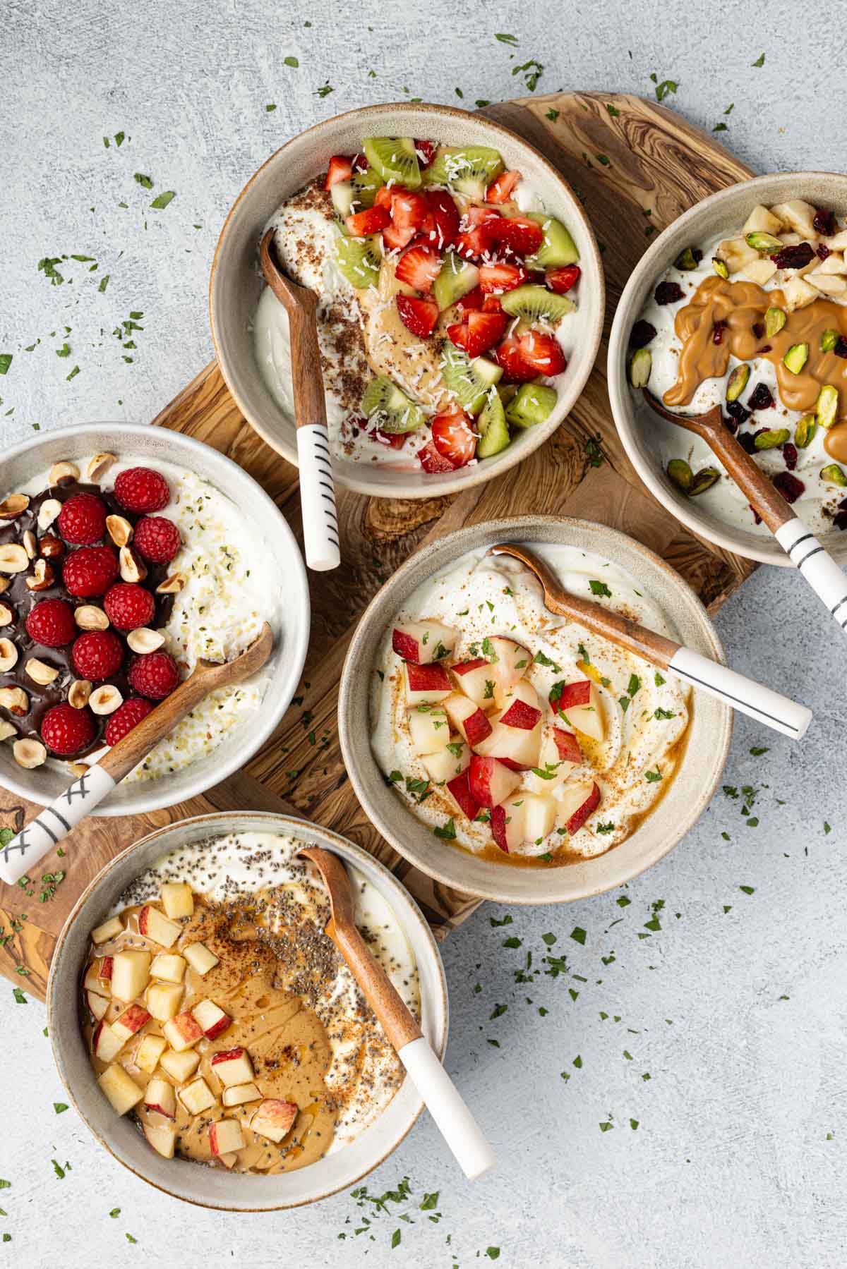 Five Greek yogurt breakfast bowls with rustic spoons.