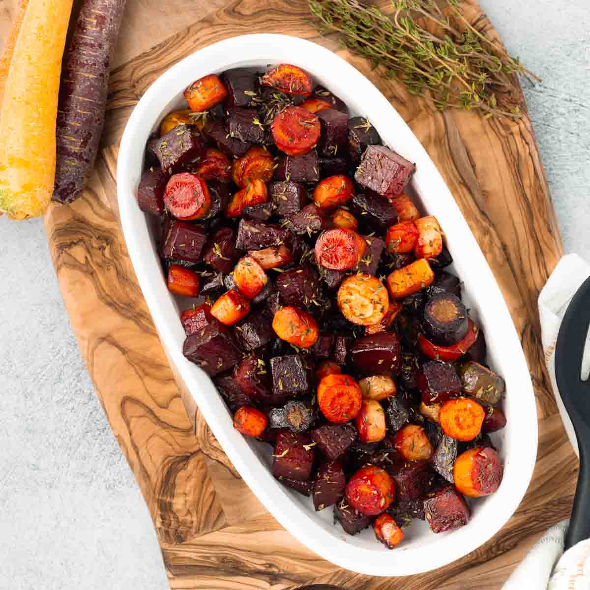 Roasted beets and carrots in a white oval serving dish, resting on a rustic wood cutting board.