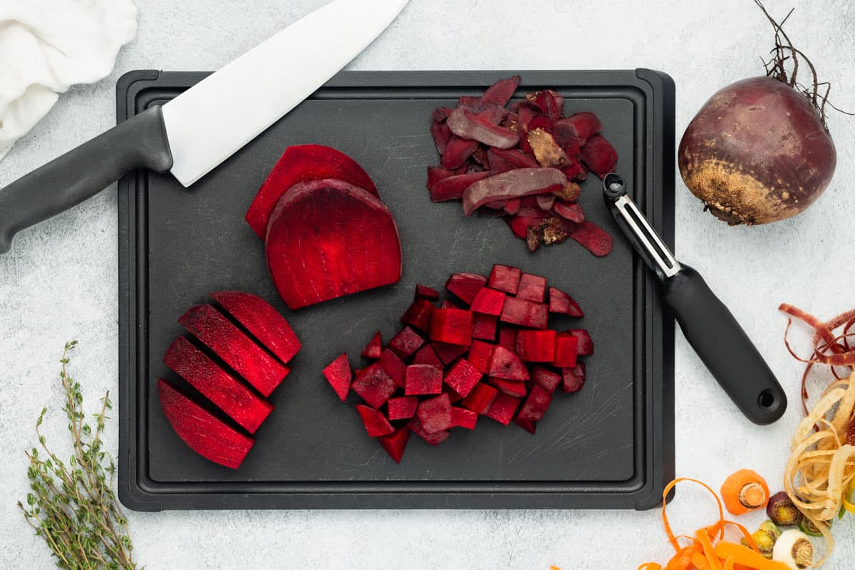 Peeled beets are sliced into wedges, strips, and cubed on a black cutting board.