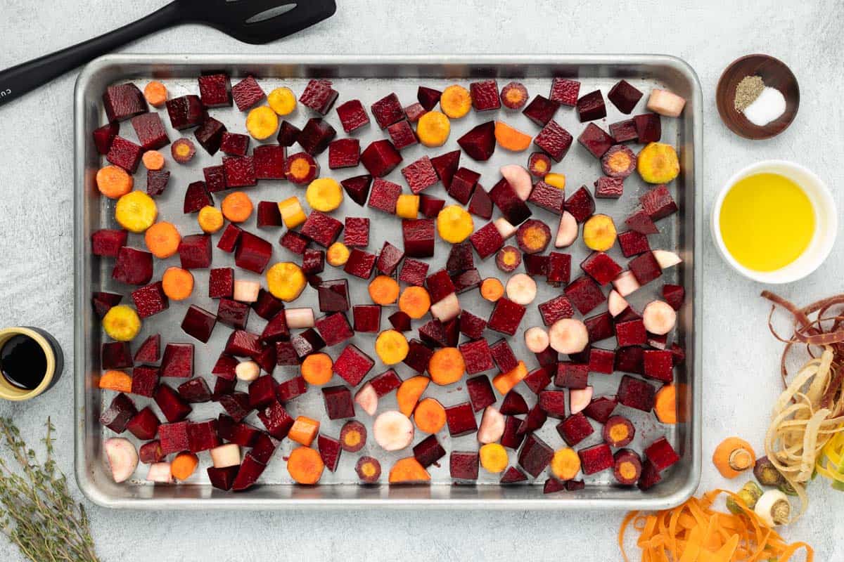 Chopped carrots and cubed beets are on a baking sheet.