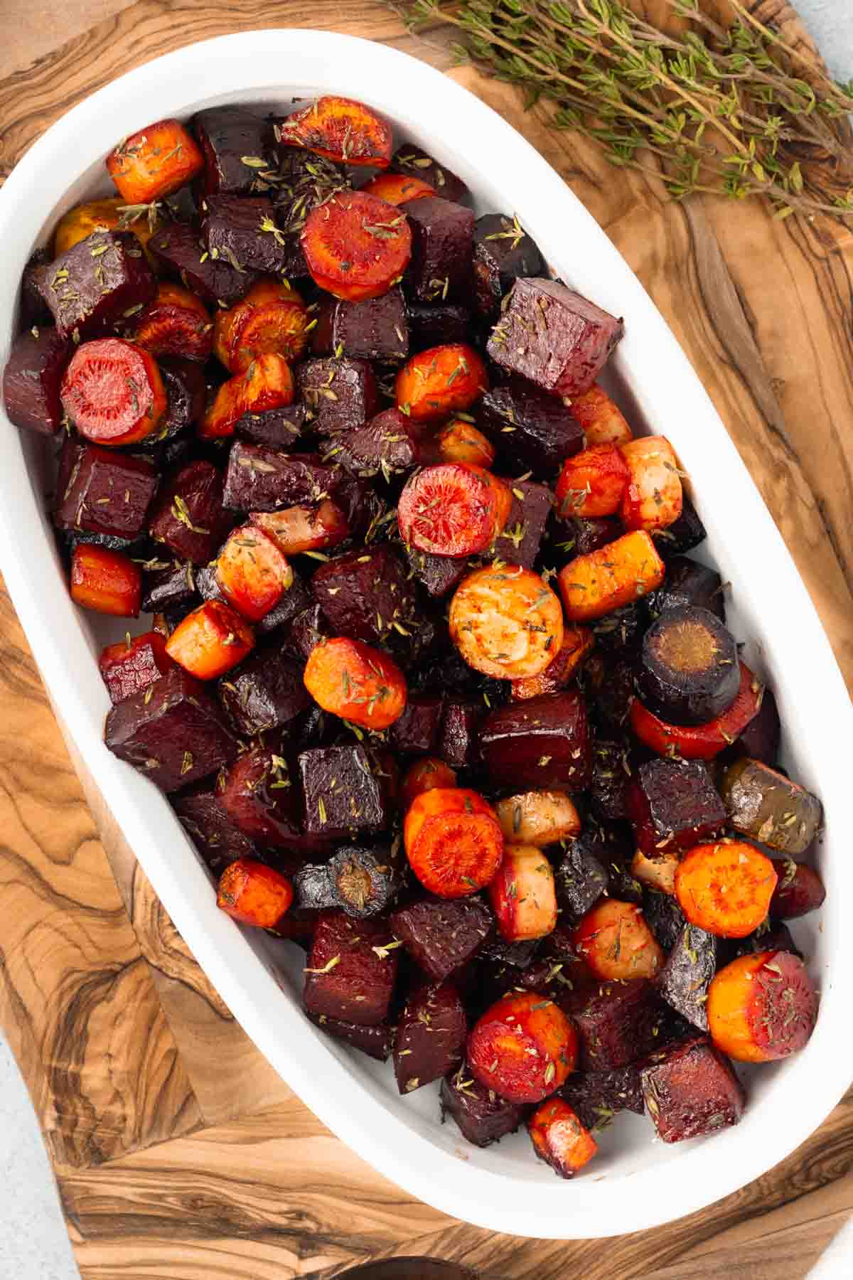 Roasted beets and carrots in a white oval serving dish, resting on a rustic wood cutting board.