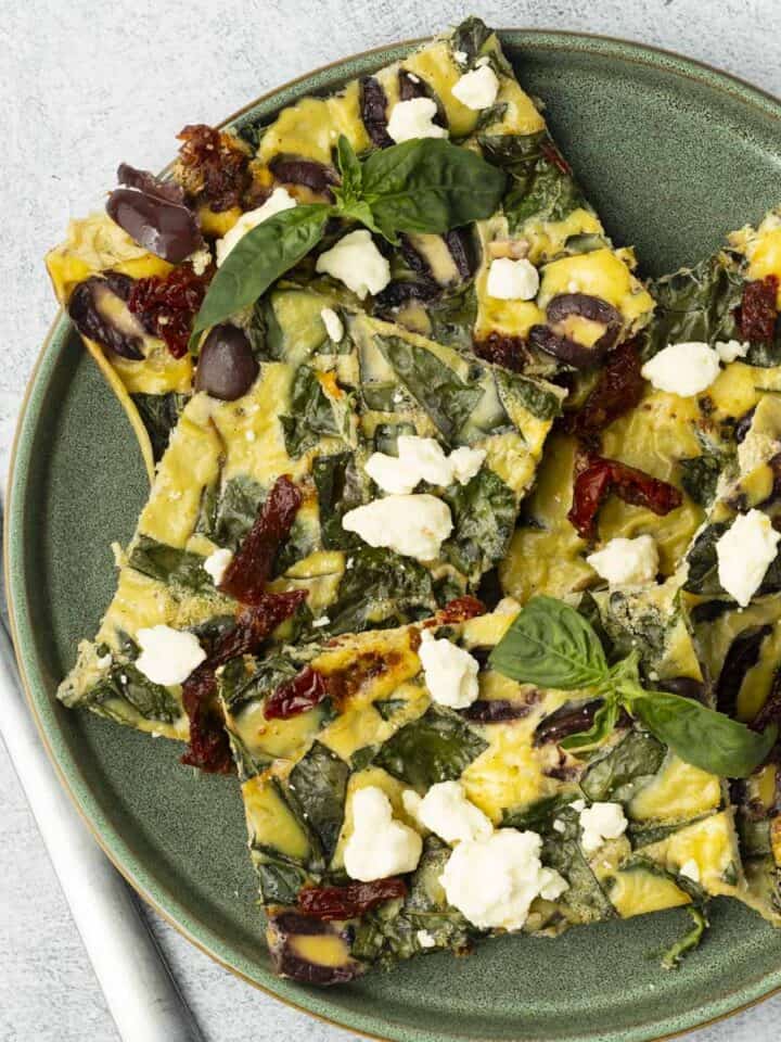 Five slices of sheet pan eggs on a green plate with fork.