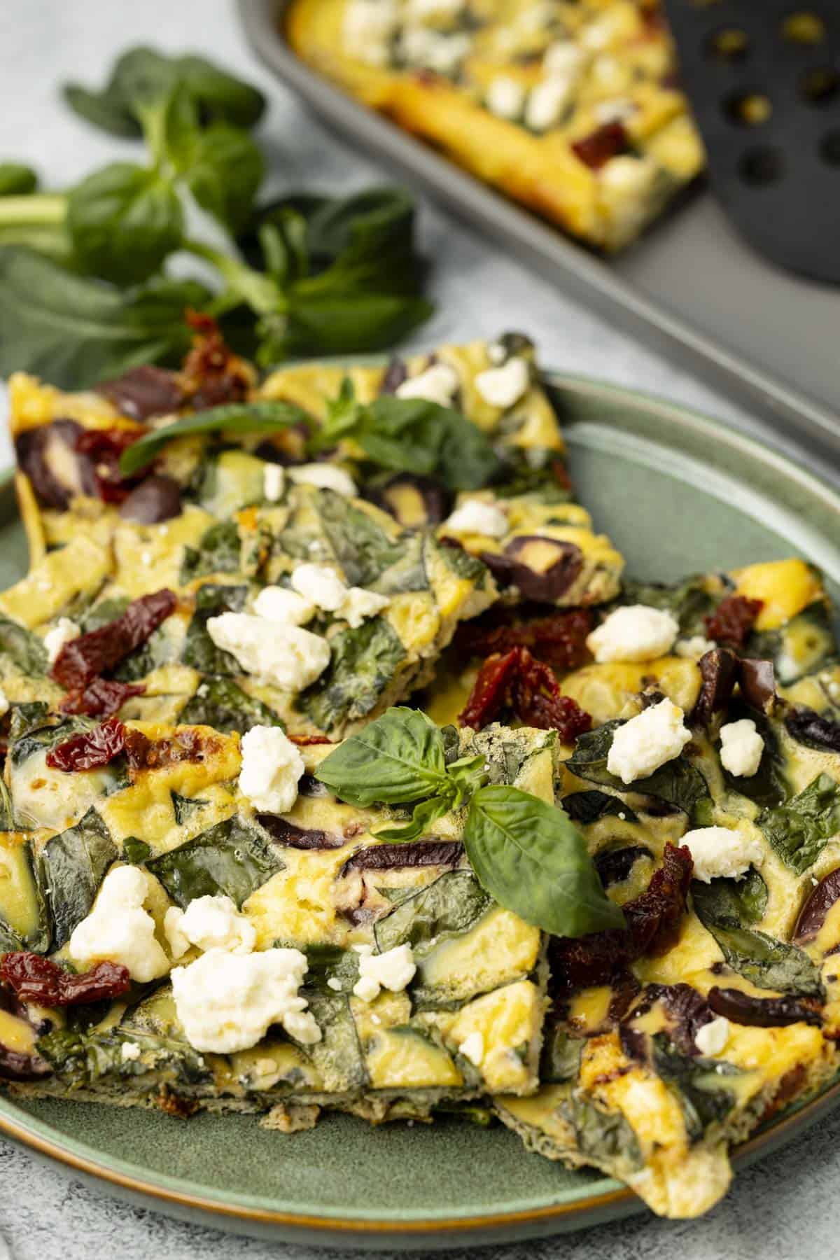 Five slices of sheet pan eggs on a green plate with fork, next to the baking sheet.