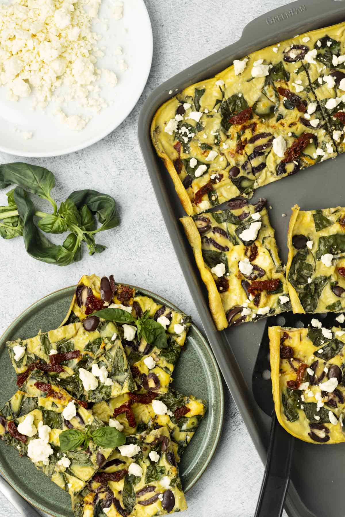 Sliced Greek-inspired sheet pan eggs on a plate next to more slices on a baking sheet.