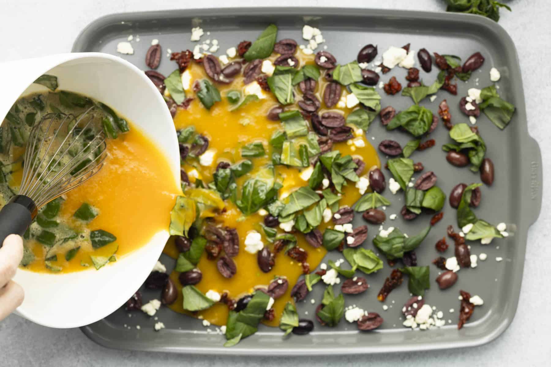 All recipe ingredients evenly spread on a baking sheet, with whisked eggs poured in.