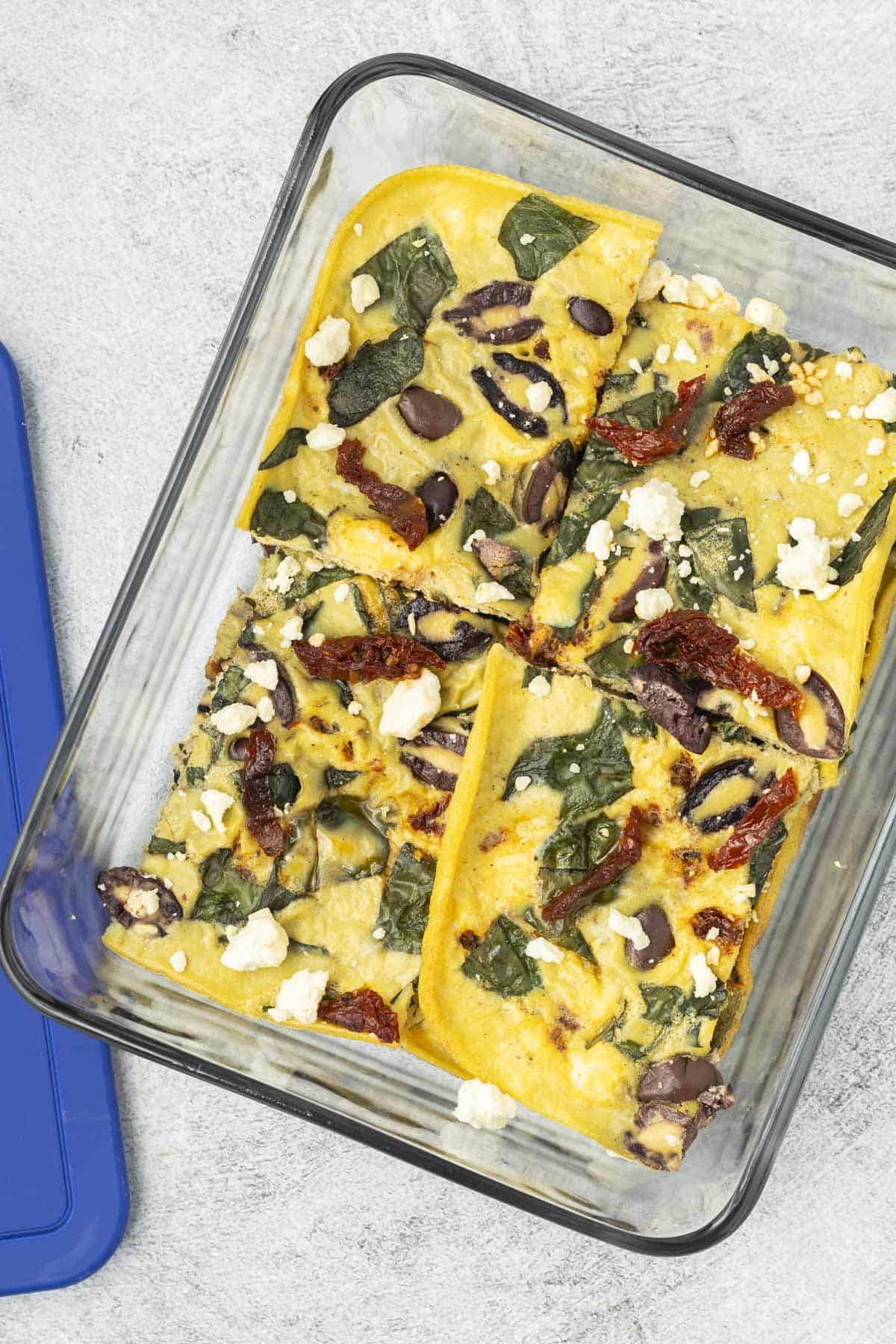 Sliced sheet pan eggs transferred to a glass storage container next to the storage lid.