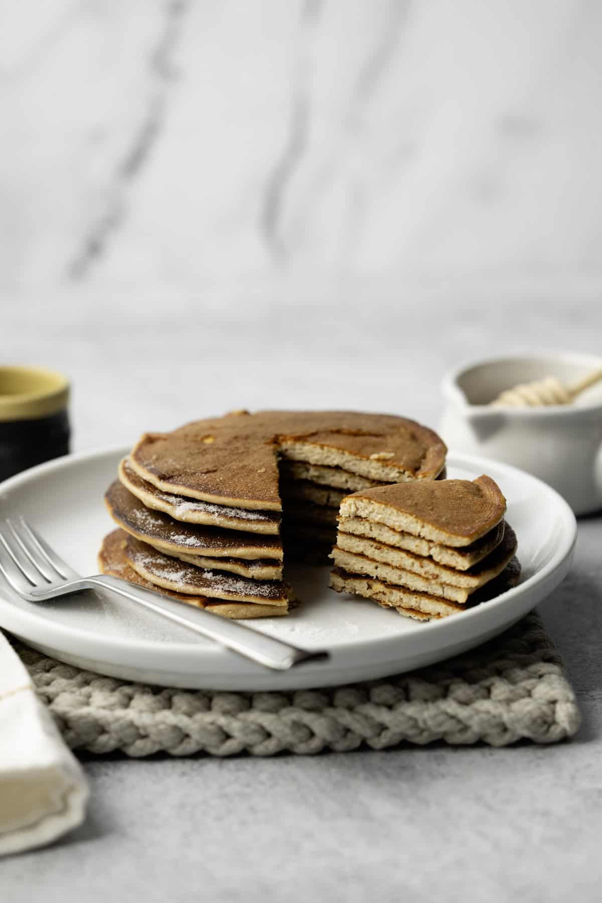 Stack of pancakes served on a white plate with fork.